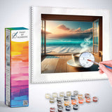 Paint by Numbers artwork showing a seaside sunrise with a steaming coffee on a wooden table and painting supplies in the foreground.