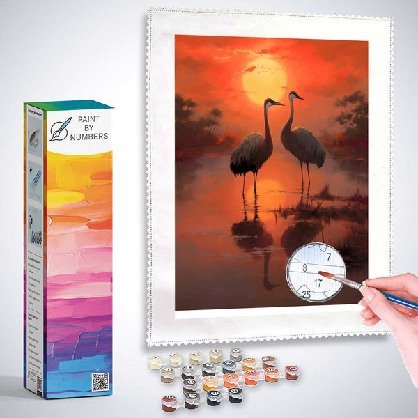 Paint by Numbers kit of two cranes at sunset with a warm red and golden sky reflecting on the water, evoking harmony and peace.