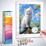 Paint by Numbers kit with a white kitten on a tree branch, surrounded by ripe apples and a bright blue sky, being painted.