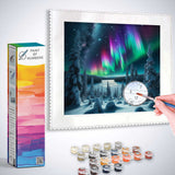 Person painting a Paint by Numbers set depicting Northern Lights over a winter forest with supplied paints.