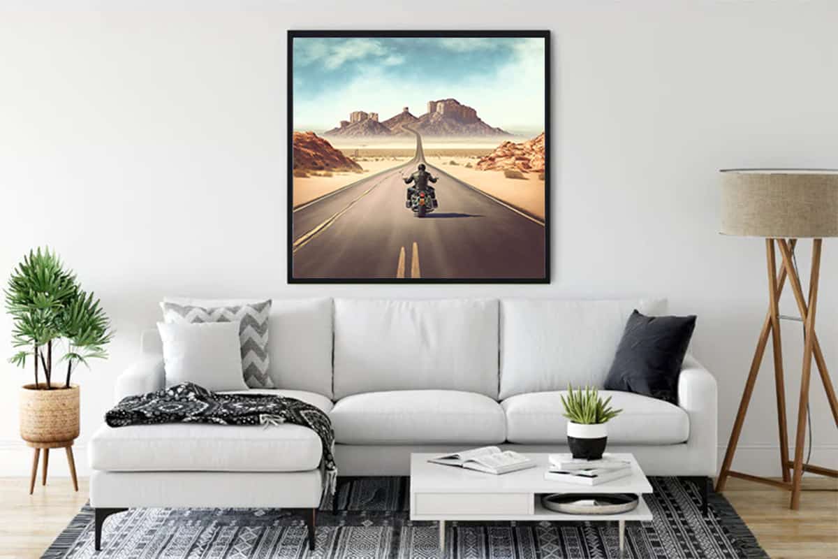 Wall art of motorcycle on desert road displayed above sofa in modern living room.