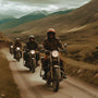 Group of motorcyclists riding dirt road through mountainous landscape