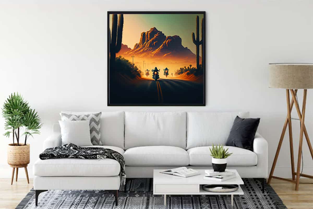 Diamond Painting - Asphalt Cowboy framed artwork featuring motorcyclist on a desert road at sunset displayed above a white sofa in modern living room.