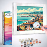 Paint by Numbers kit featuring Riviera Träume coastal town artwork with vibrant orange and azure hues, paint set, and brush in hand