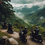 Bikers riding motorcycles on a scenic mountain road surrounded by lush greenery and misty hills.