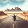 Motorcyclist riding down desert highway towards distant mountains under a blue sky.