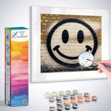 Paint by Numbers canvas kit featuring a smiley face graffiti on a yellow brick wall with painting supplies shown.